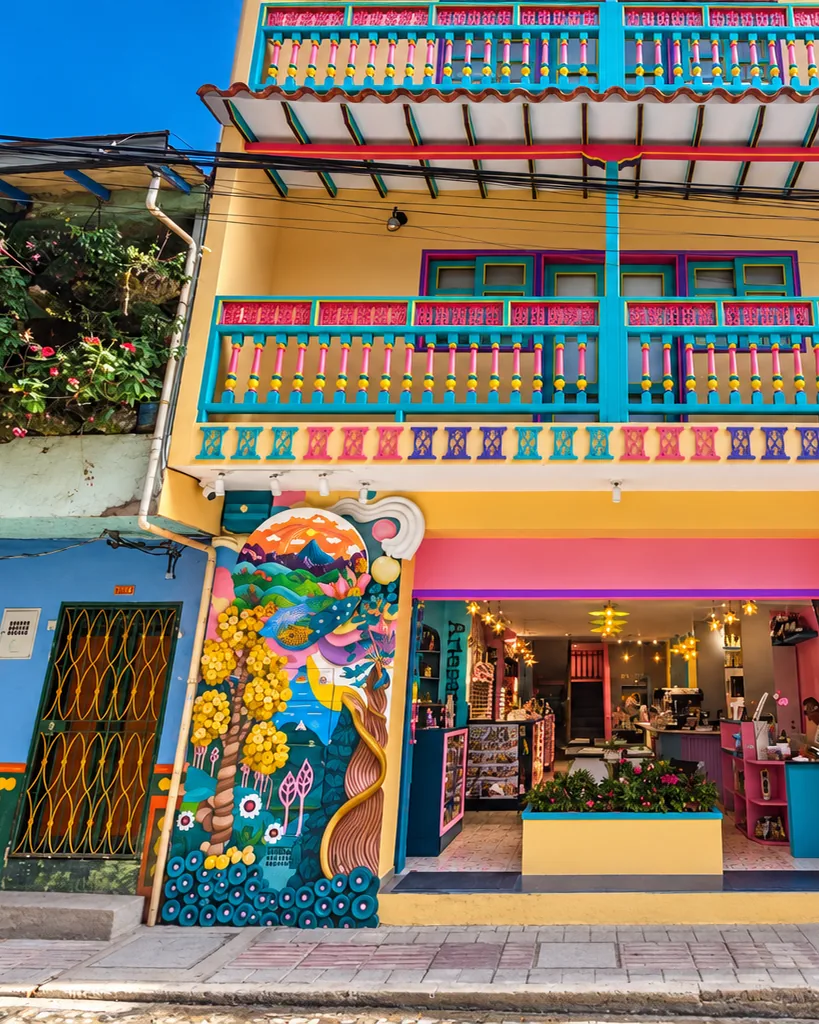 Façade of a hotel in central Guatapé, painted yellow, pink and turquoise, with balconies and zócalos.
