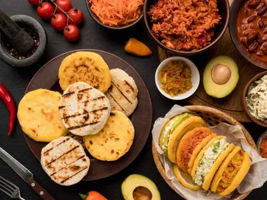 Arepas, chorizo, huevo y aguacate servidos sobre una mesa de madera.