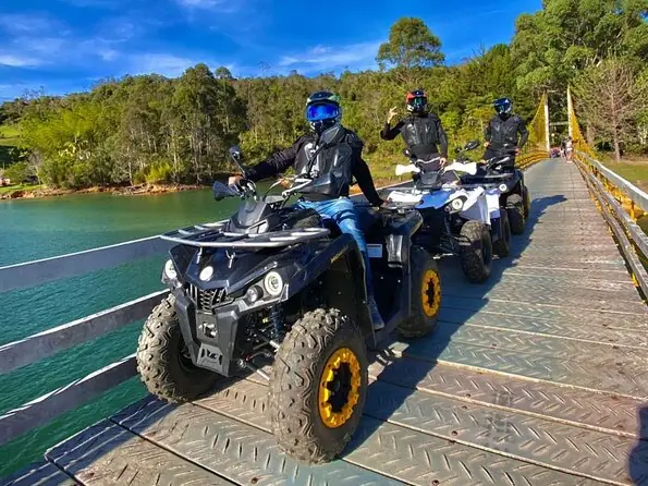Tres cuatrimotos cruzando un puente de madera junto al embalse.