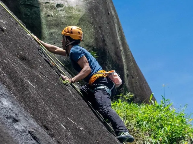 Un escalador con casco subiendo por la pared de roca.