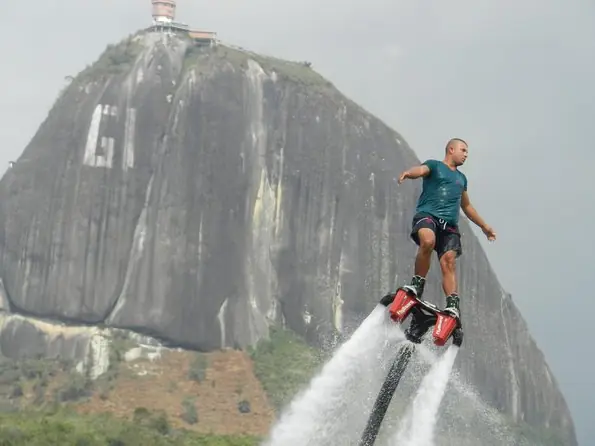Una persona elevada sobre el agua con un flyboard, con el Peñón detrás.