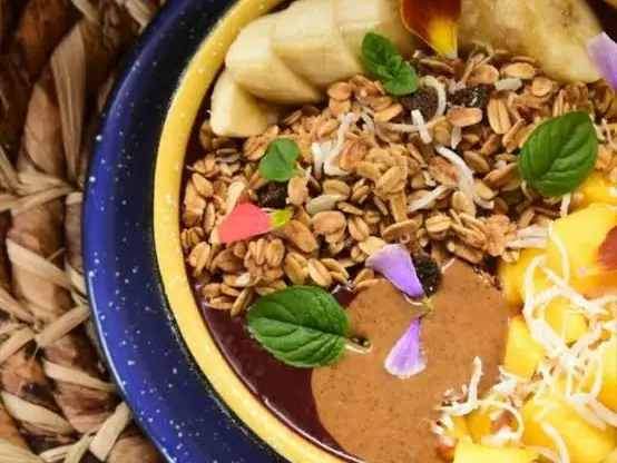 Un bowl de frutas con granola, banano y mango en un plato azul.