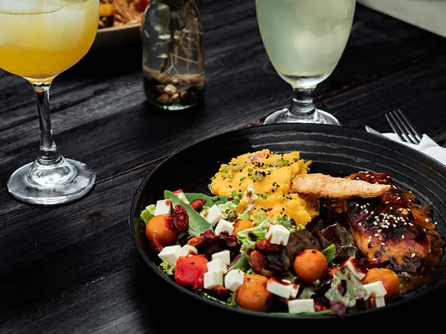 Un plato de cocina internacional con salmón, ensalada y dos cocteles.
