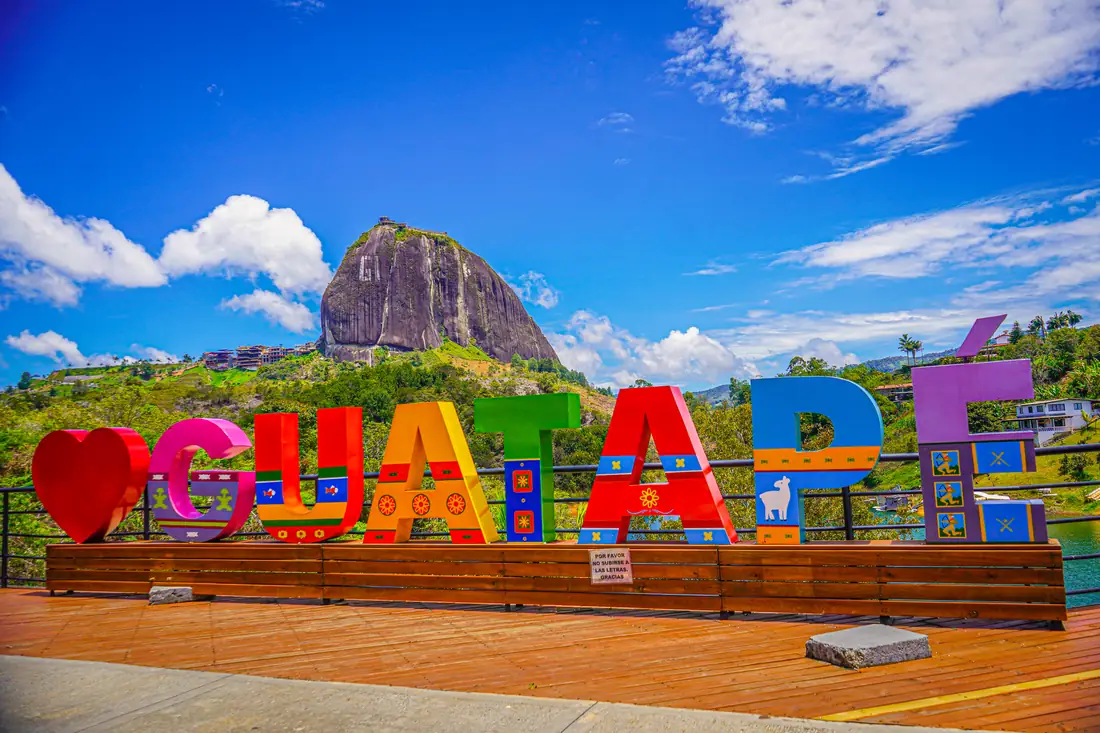 The colourful letters of the Guatapé sign with El Peñón behind.