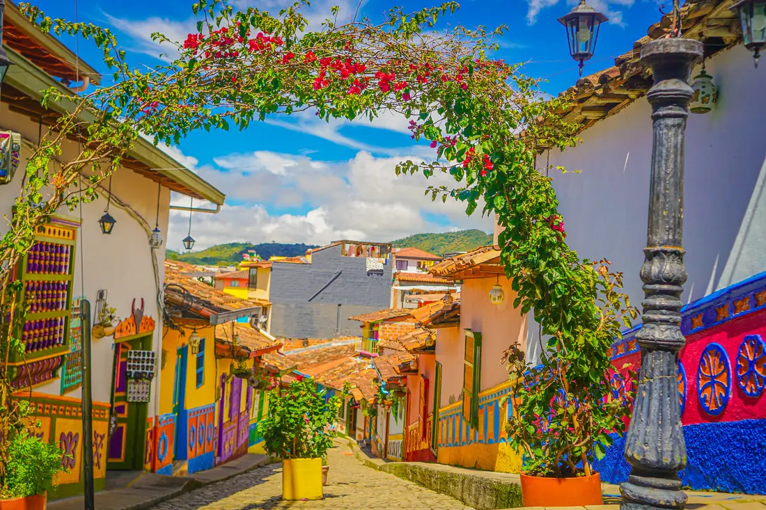 A cobbled street in Guatapé with colourful façades, painted zócalos and a bougainvillea in bloom.