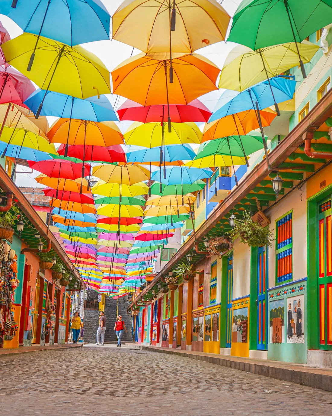 La Calle de las Sombrillas de Guatapé, empedrada y cubierta por sombrillas de colores, con zócalos pintados en las fachadas.